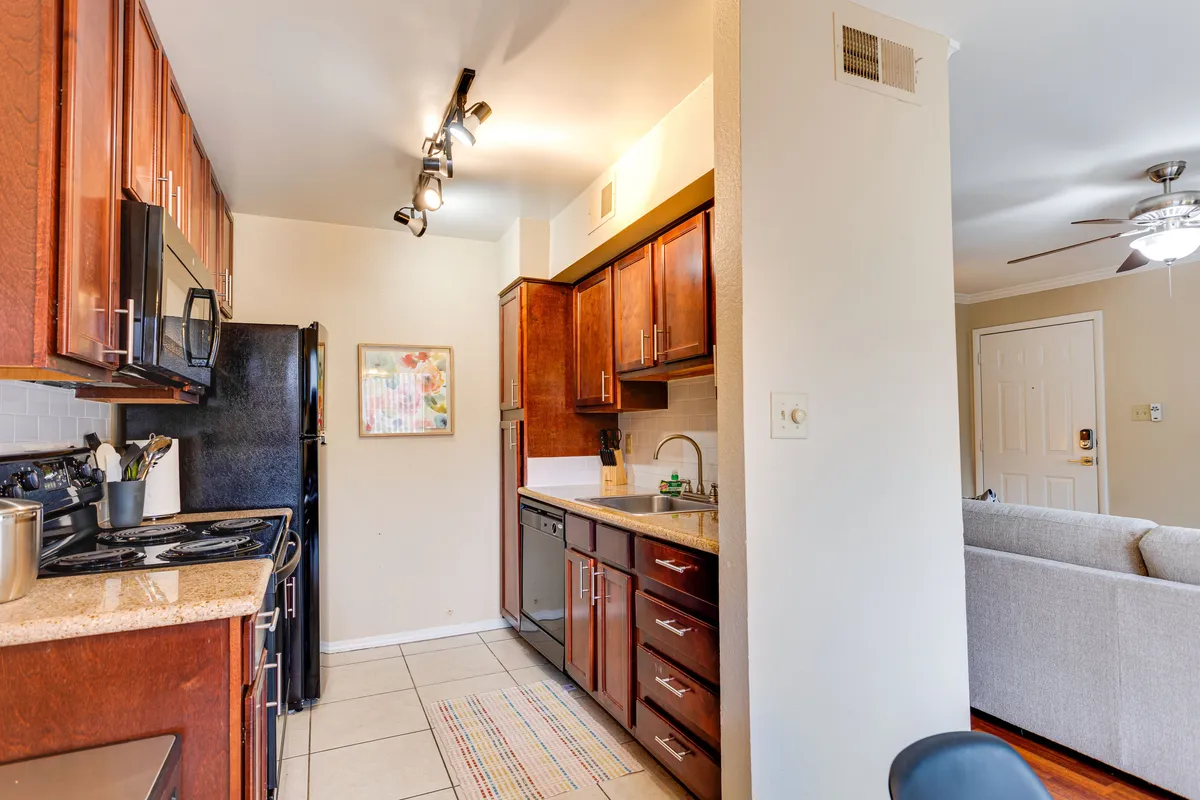 A modern kitchen with granite countertops, stainless steel appliances, wooden cabinetry, and colorful artwork. The space is lively and functional, perfect for cooking, entertaining, or simply starting the day with a coffee.
