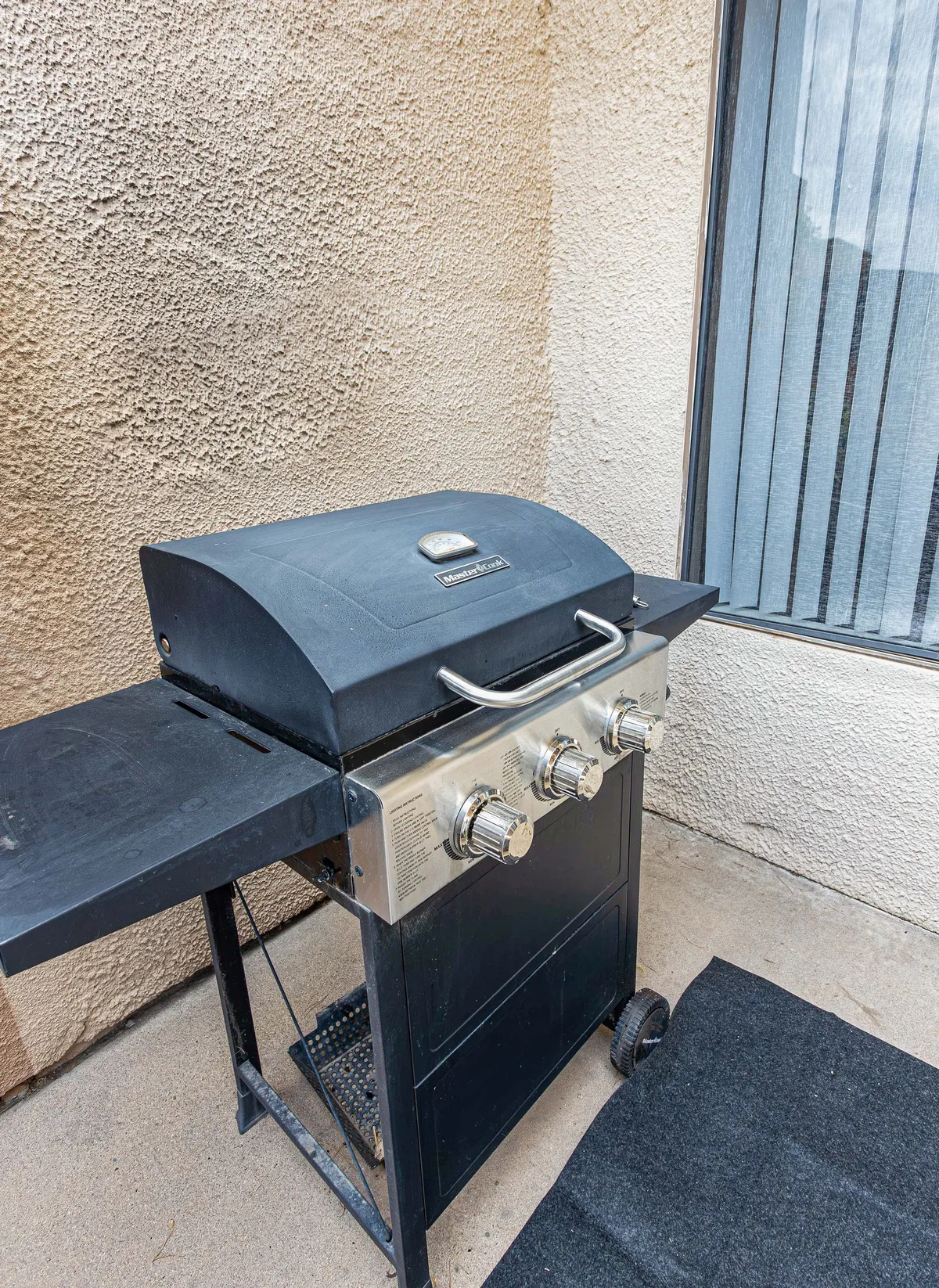 A dedicated outdoor grilling area is the focal point here, featuring a modern BBQ grill set against a private exterior backdrop. This casual outdoor space is complemented by nearby seating and a window, suggesting immediate access to indoor areas.
