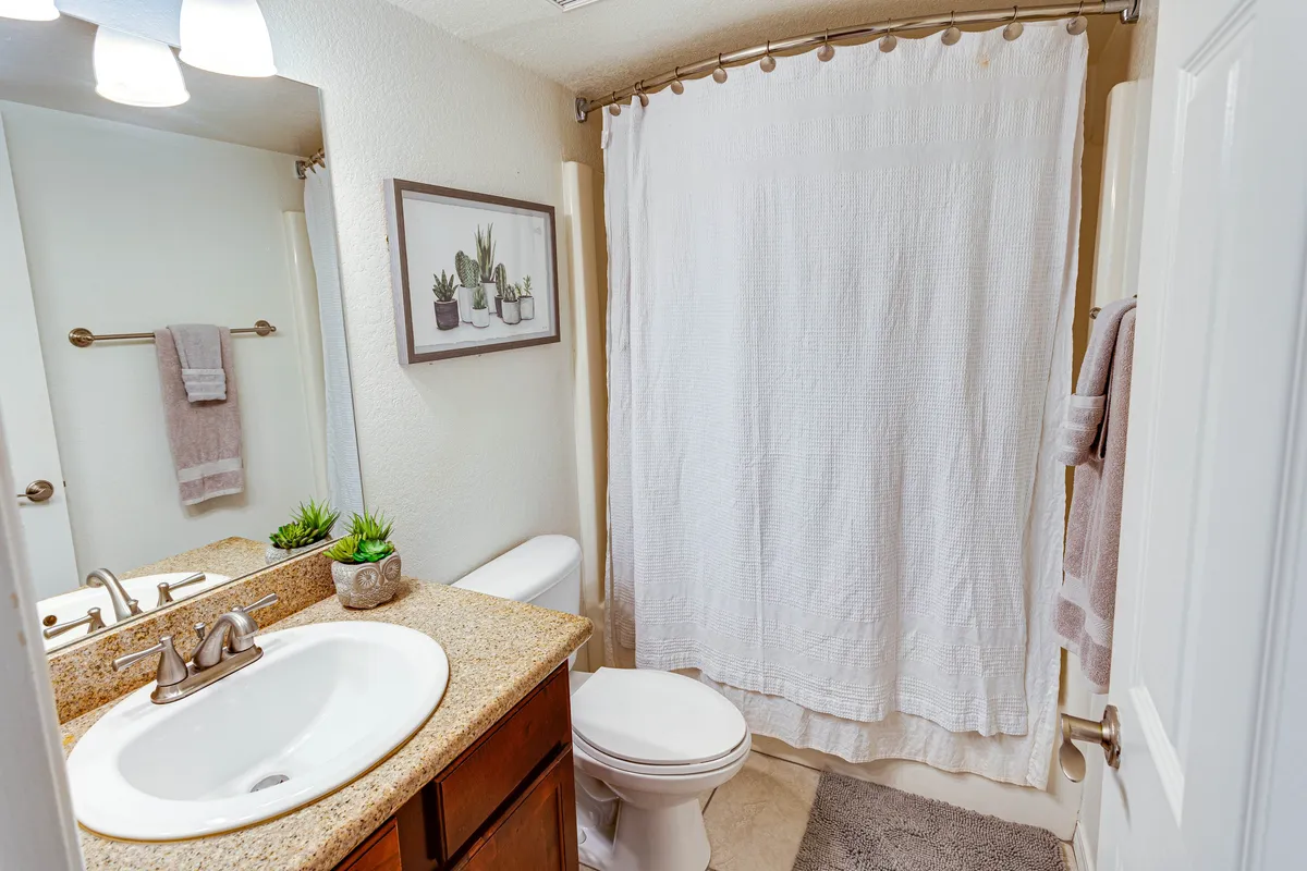 A bathroom vanity with a sink, decorative wall art, lush plants, and a shower curtain hinting at a tub/shower combo. The space feels calm and rejuvenating, inviting moments of self-care and solitude.