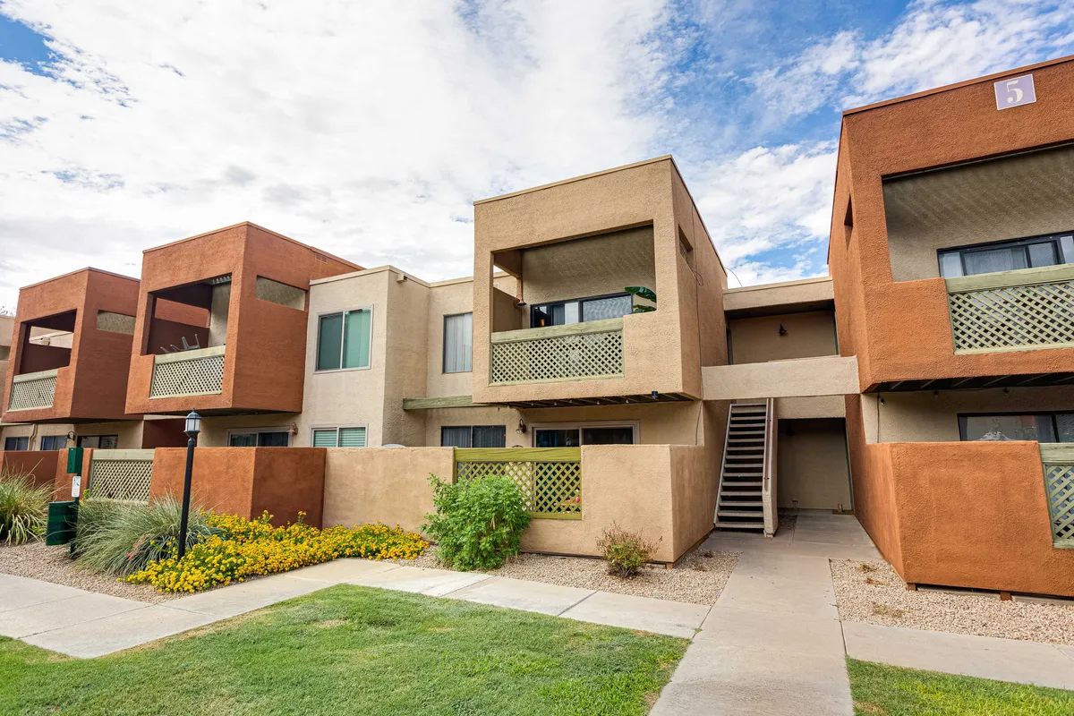 Colorful apartment facades with green balcony railings overlook well-maintained landscaping. People are seen socializing on balconies and walking amidst the gardens, creating a relaxed, welcoming vibe.