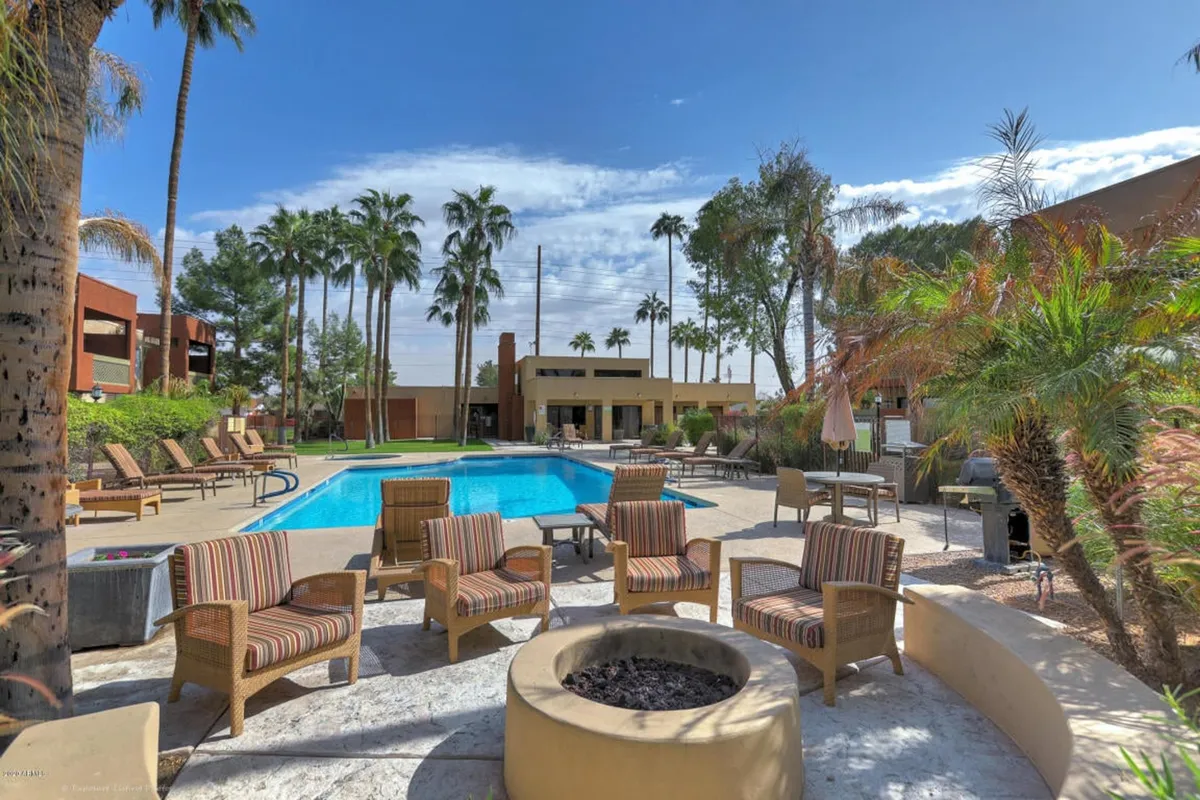 This exterior shot captures a vibrant pool area featuring a sparkling swimming pool, several lounge chairs, a cozy fire pit, palm trees, and a spacious patio. The open setting is ideal for both sunbathing and social gatherings, while the fire pit area suggests opportunities for relaxing evenings.