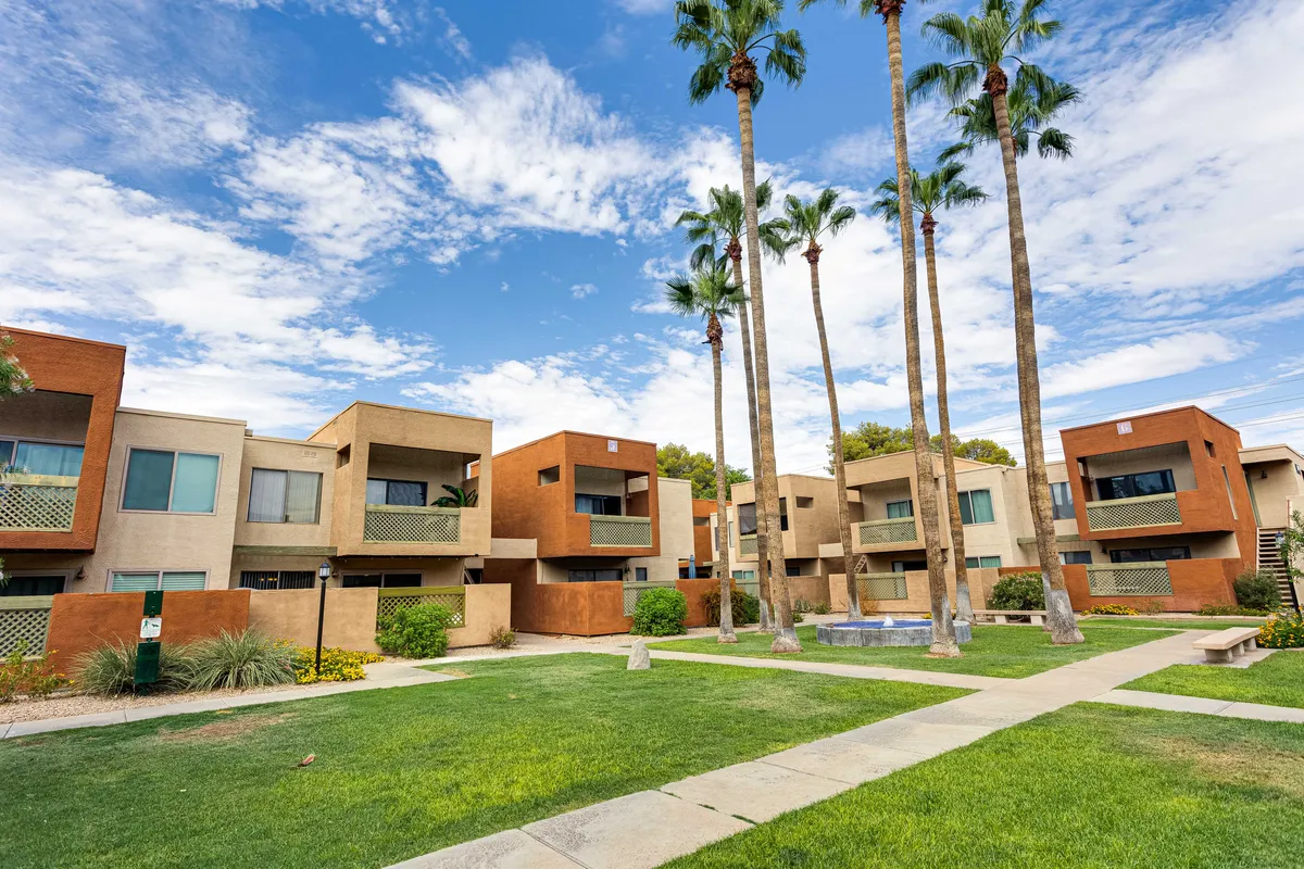 A tranquil exterior featuring palm trees, apartment buildings, a lush lawn, and a water feature, all under soft natural light. The environment looks peaceful, perfect for reflective breaks or a quick stroll to clear the mind between meetings.