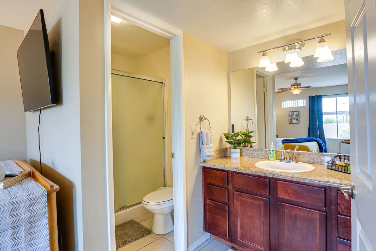 A modern bathroom with a spacious walk-in shower, sleek vanity, large mirror, and a television nearby. Clean lines and fresh decor evoke a spa-inspired feel, perfect for morning and evening routines.
