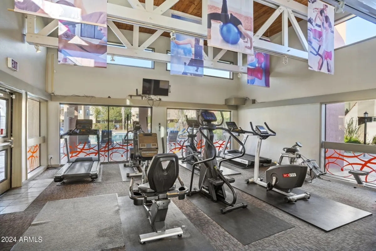 An airy, well-equipped fitness center featuring treadmills, elliptical machines, exercise mats, large windows that let in natural light, and colorful decorative banners. The setup encourages an active lifestyle and group or solo workouts within the community.